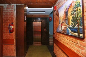 A hallway with a brick wall, a fire extinguisher, a door leading to an elevator, and a mural on the right wall.