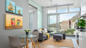 A modern living room with a glass dining table, grey sofas, and a large window offering a city view. - The Sentinel 1310 (Cape Town)