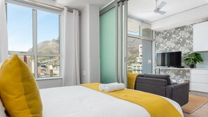A modern hotel room with a large bed, a sofa, a TV, and a view of a cityscape. - The Sentinel 1310 (Cape Town)