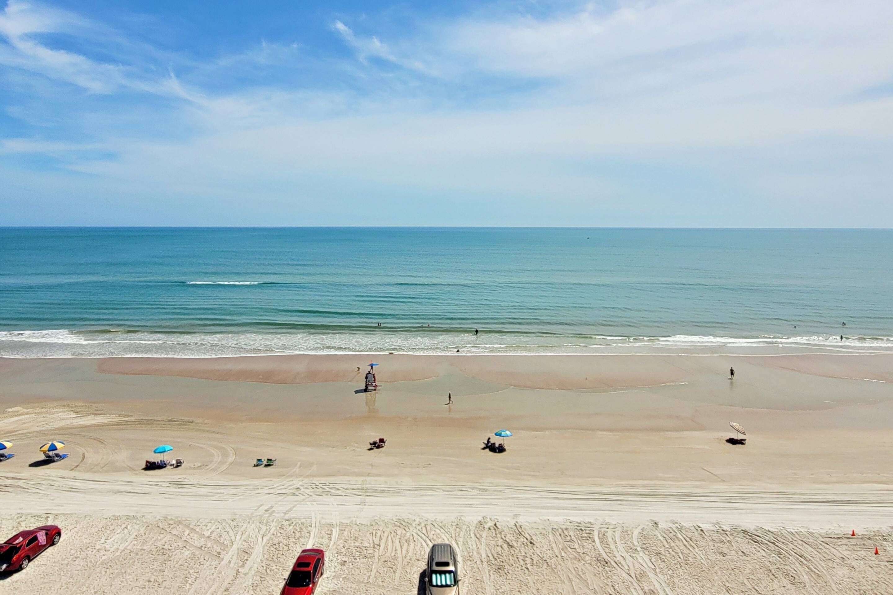 A beach with a clear sky, calm sea, and several umbrellas.