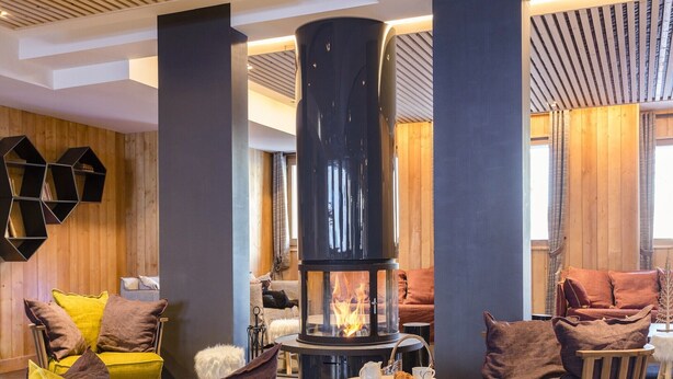 A modern interior with a central fireplace, wooden panel walls, and a variety of seating arrangements. - Modern Comfort by the Slopes (Tignes 1800)