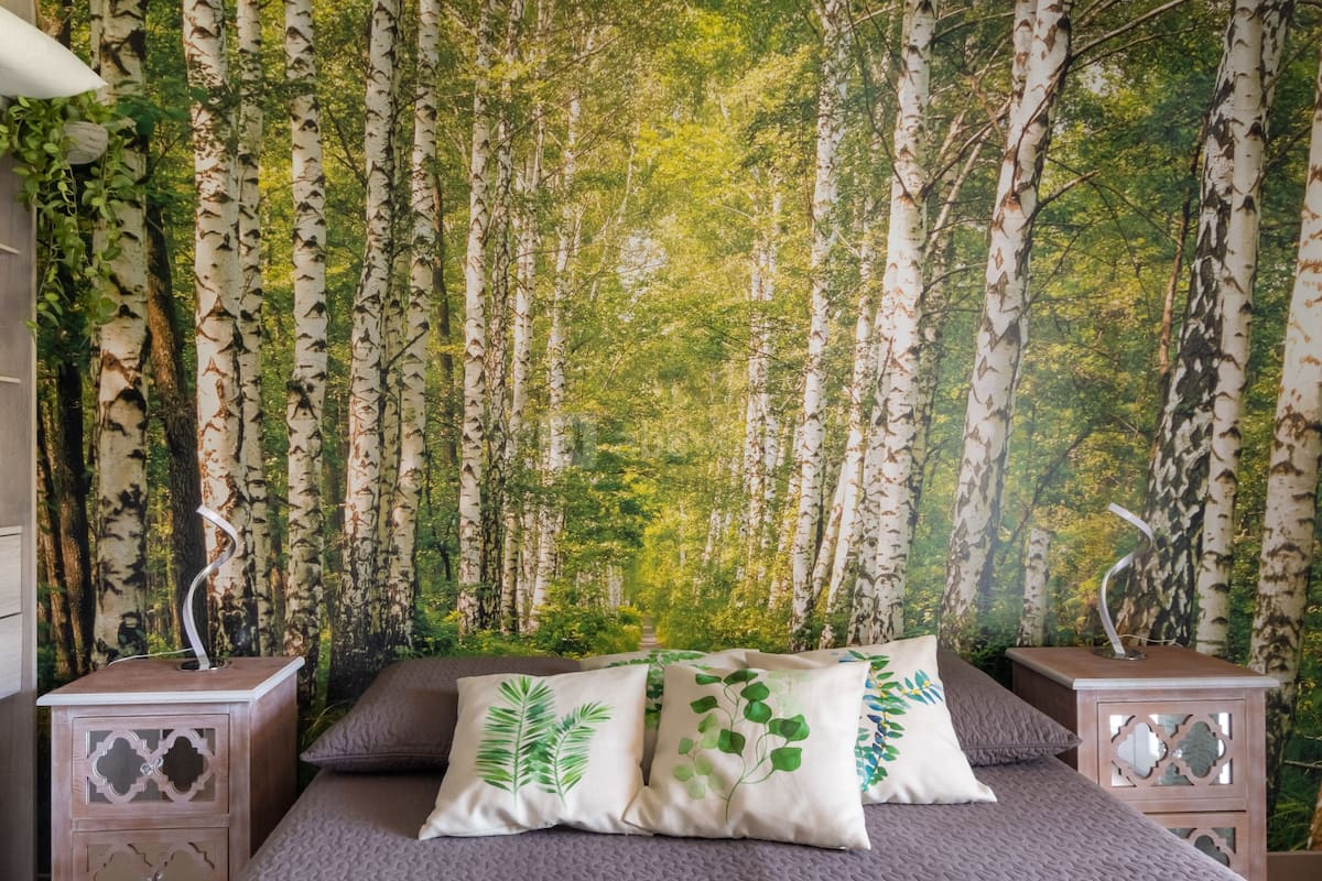 A bedroom with a bed, two nightstands, and a forest-themed wall tapestry.