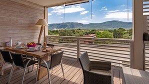 A balcony with a wooden table, chairs, and a view of a mountainous landscape. - Cosy apartment for 2 guests with WIFI, pool, A/C, TV and terrace (Porto-vecchio)