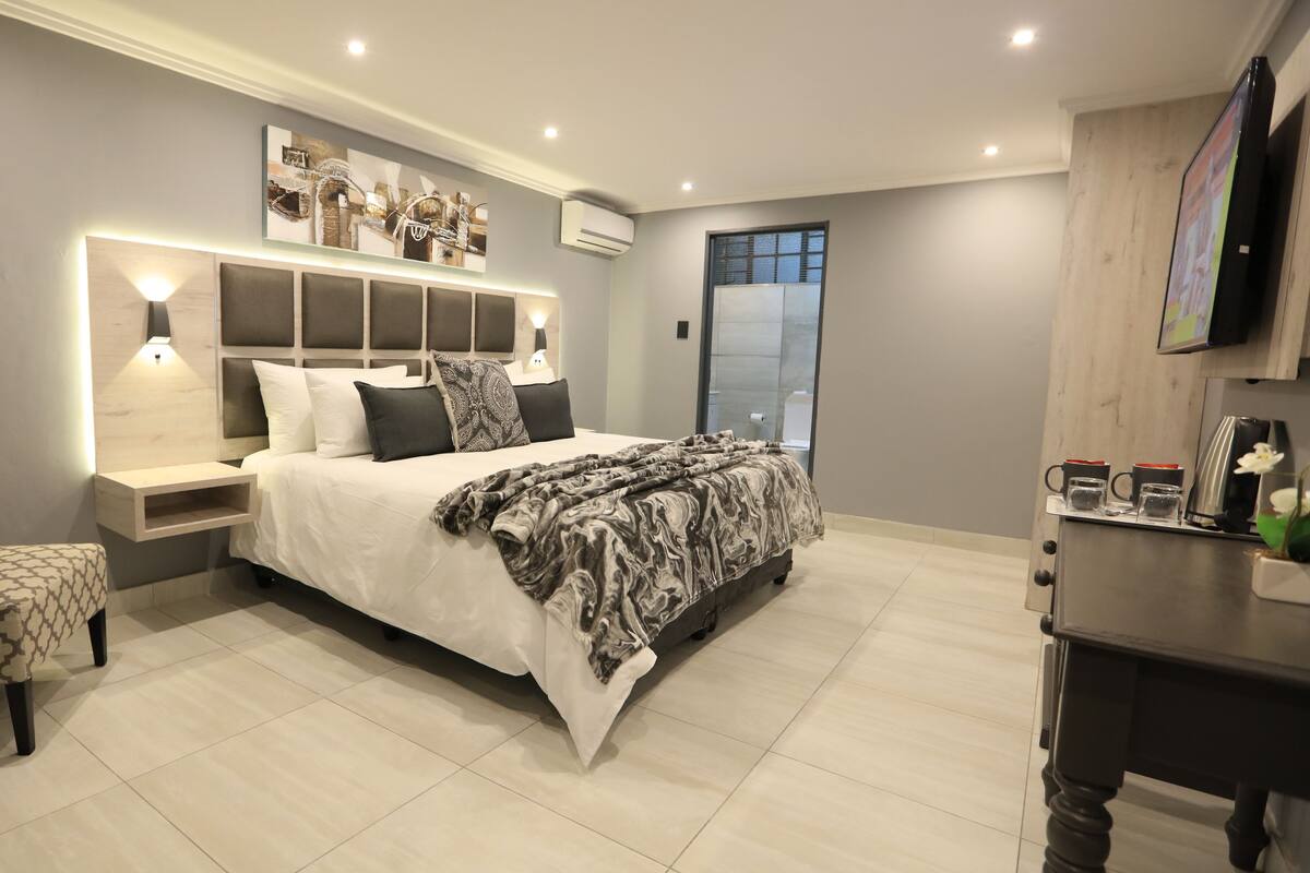 A modern bedroom with a large bed, bedside tables, a chair, and a coffee machine.