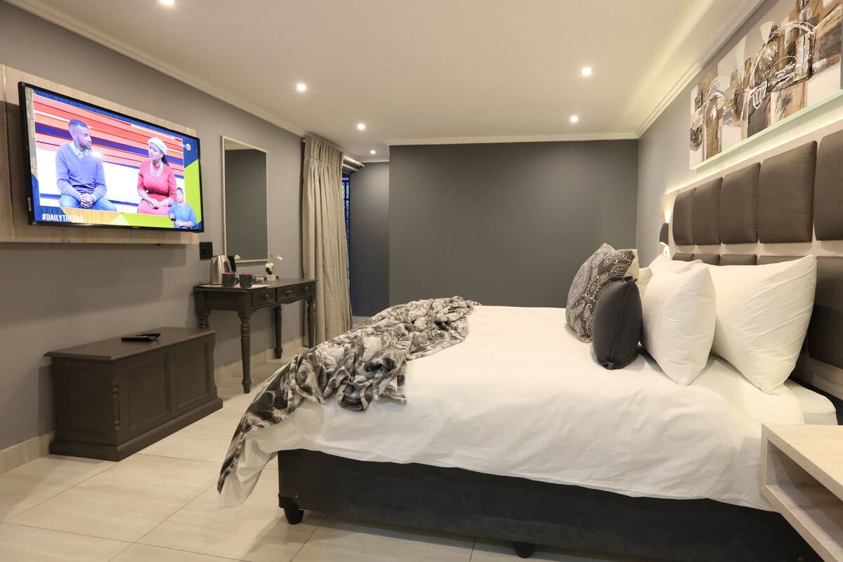 A modern bedroom with a large bed, a TV mounted on the wall, a bedside table, and a nightstand.