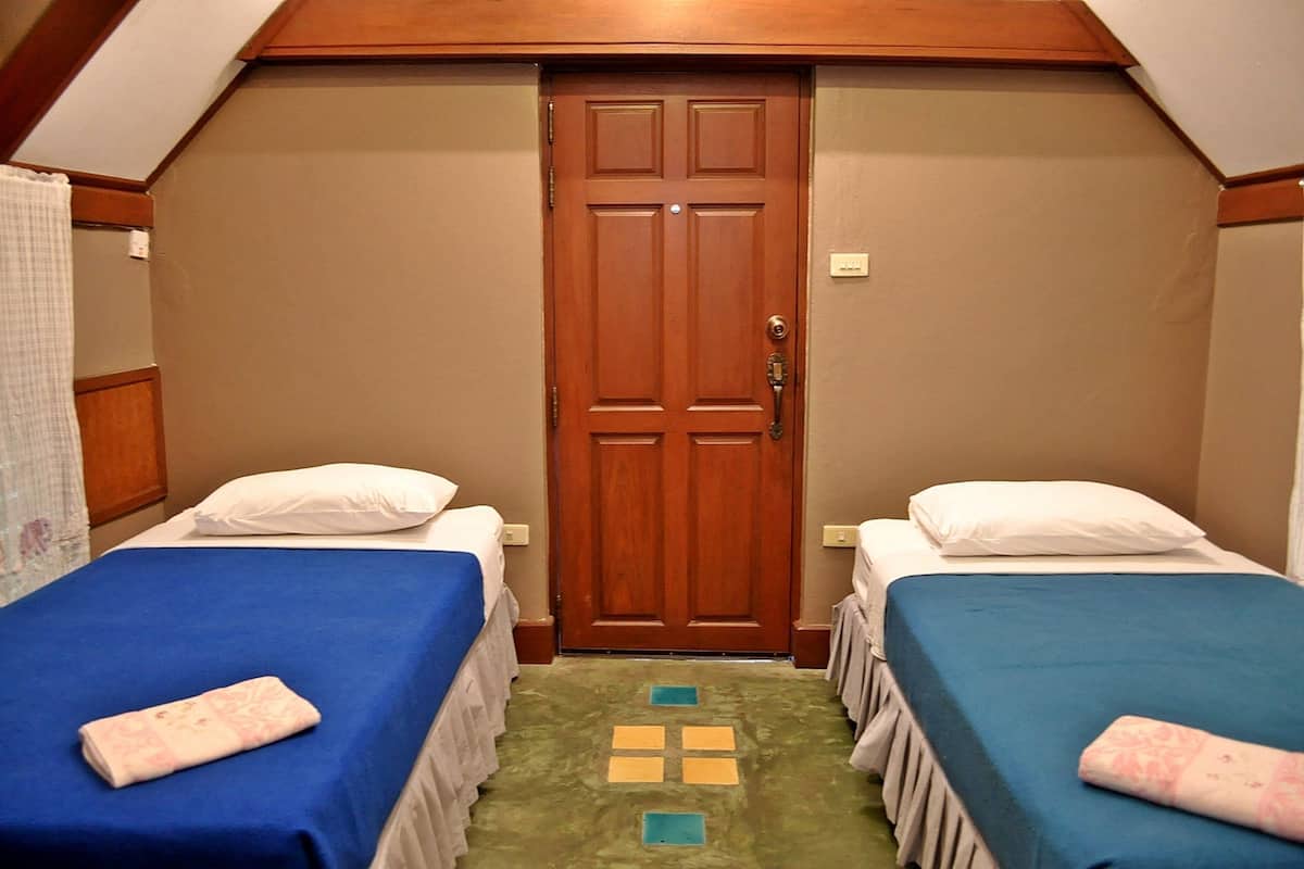 Una habitación con dos camas individuales, una puerta de madera y una ventana pequeña.