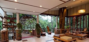 Een ruime lobby met houten meubels, potplanten en bewegwijzering.