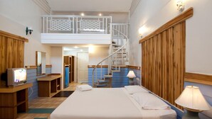 Une chambre à coucher comprenant un lit, une télévision, un bureau, une lampe et un escalier menant à un niveau supérieur.