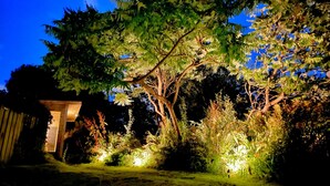A well-lit garden area with a large tree and various plants illuminated by garden lights. - Romantic, quirky, unique cottage, big garden, free parking, pet friendly max 2 (Beckermet)