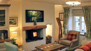 A cozy living room with a fireplace, a comfortable sofa, a wooden coffee table, and a bookshelf. - Romantic, quirky, unique cottage, big garden, free parking, pet friendly max 2 (Beckermet)