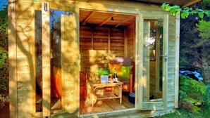 A wooden cabin with a glass door, a small table with a bottle and glasses, and a bench. - Romantic, quirky, unique cottage, big garden, free parking, pet friendly max 2 (Beckermet)