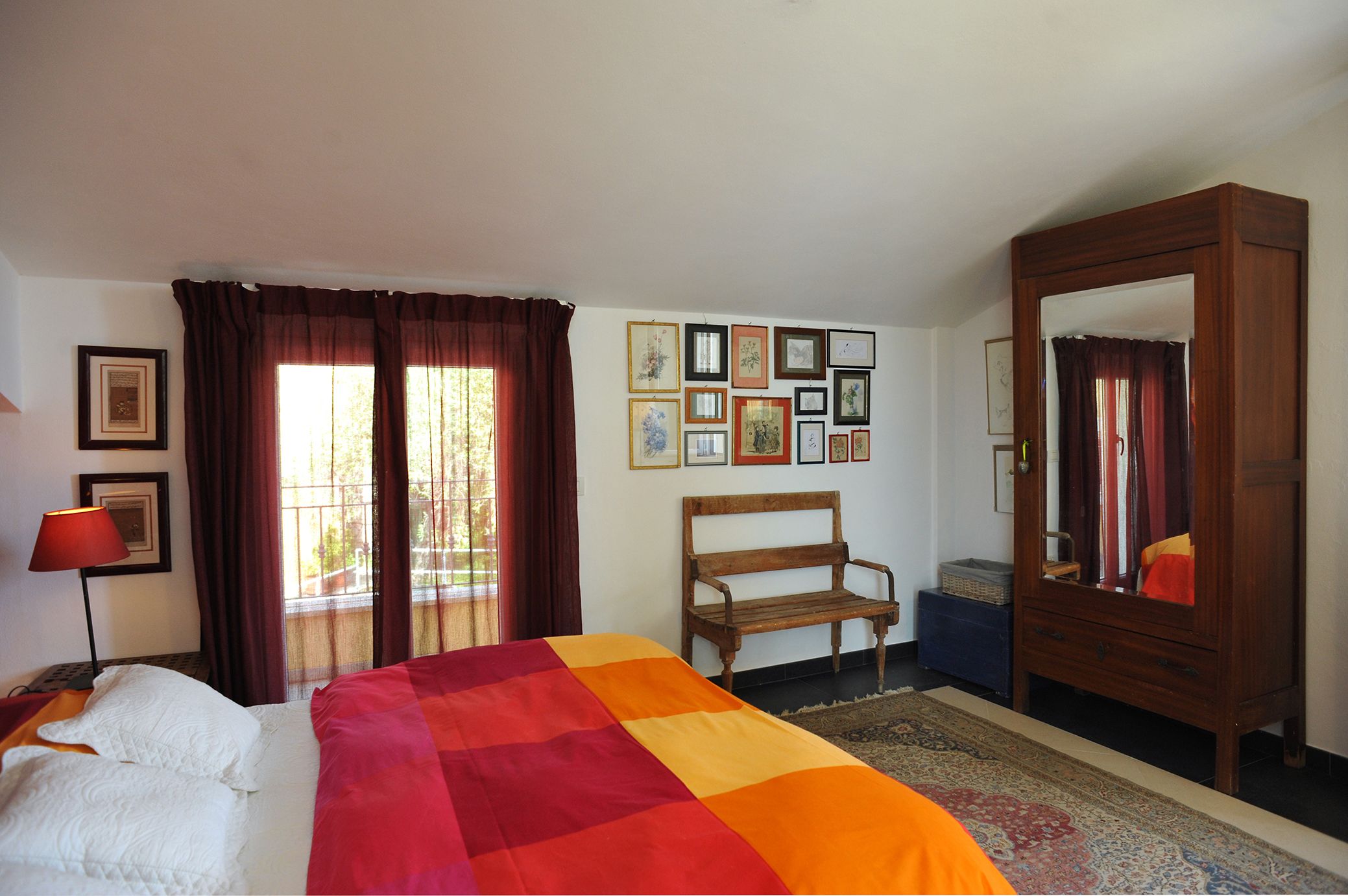 Una camera d'albergo con un letto, una panca, un armadio e una parete con quadri.
