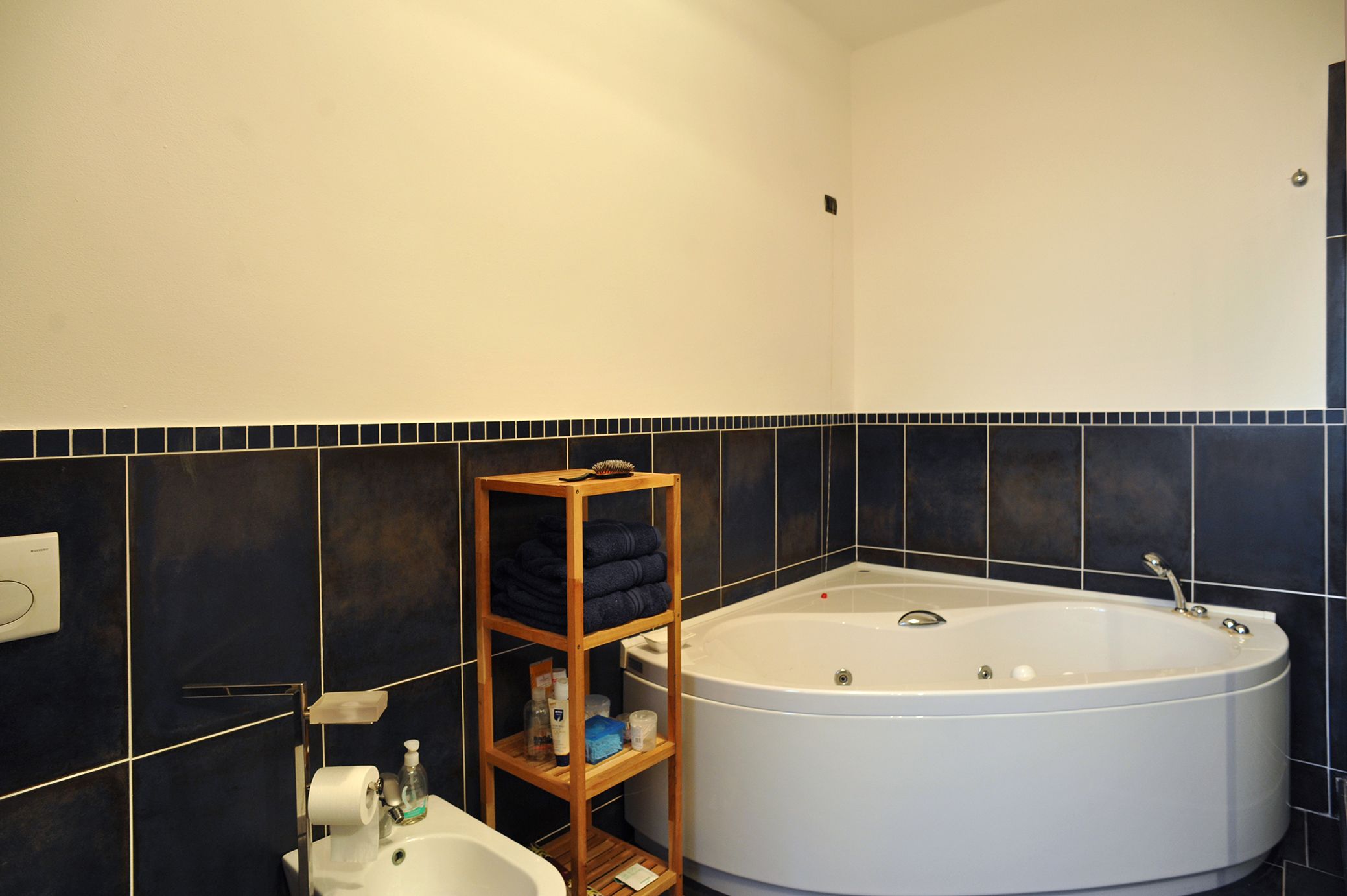 Un bagno con una vasca, uno scaffale di legno con asciugamani, un water e un lavandino.