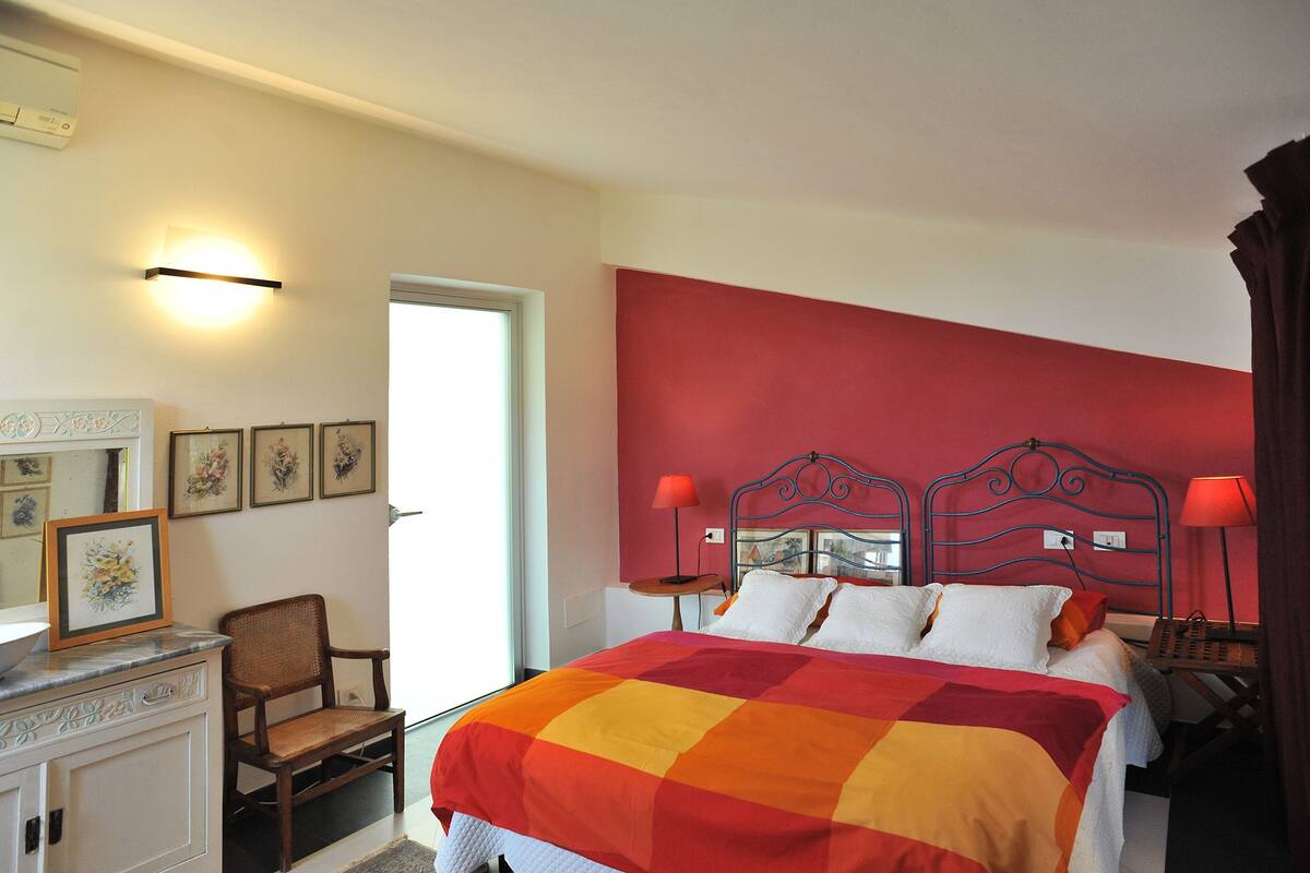 Une chambre d’hôtel avec un lit, deux tables de chevet avec des lampes, une chaise, un bureau avec un miroir et des tableaux encadrés accrochés au mur.