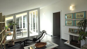 A modern living room with a glass door leading to a balcony, a lounge chair, and a bookshelf.