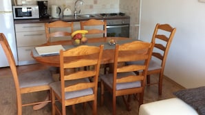 A compact kitchen with a dining table and chairs, a microwave, and a stove. - Apartmani KLIM (Dubrovnik)