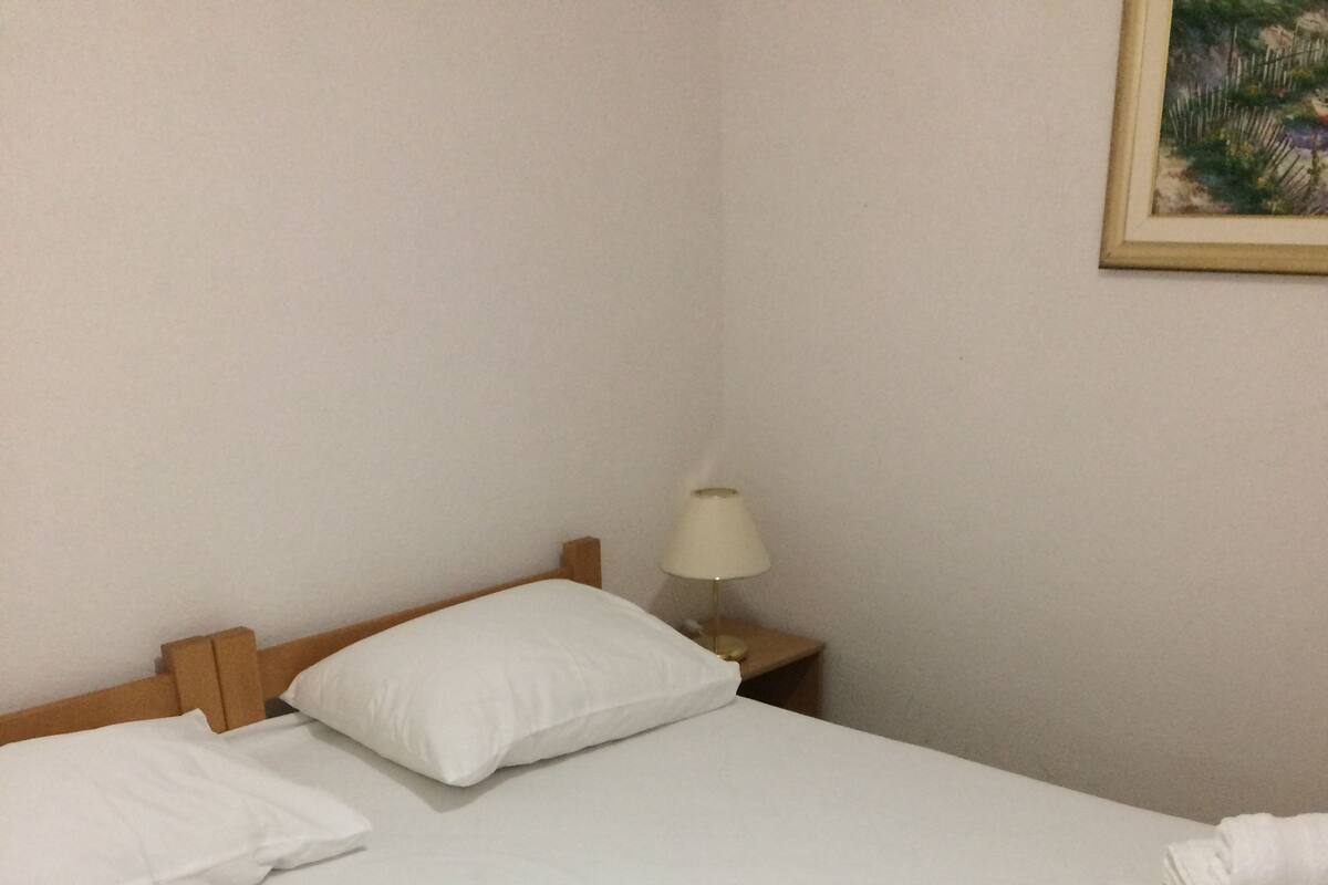 A neatly made bed with white linens, a bedside lamp, and a rolled towel on the bed.