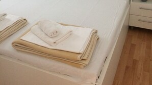 A neatly made bed with white linens and a folded beige towel, a bedside table with a lamp, and a wooden floor. - Apartmani KLIM (Dubrovnik)