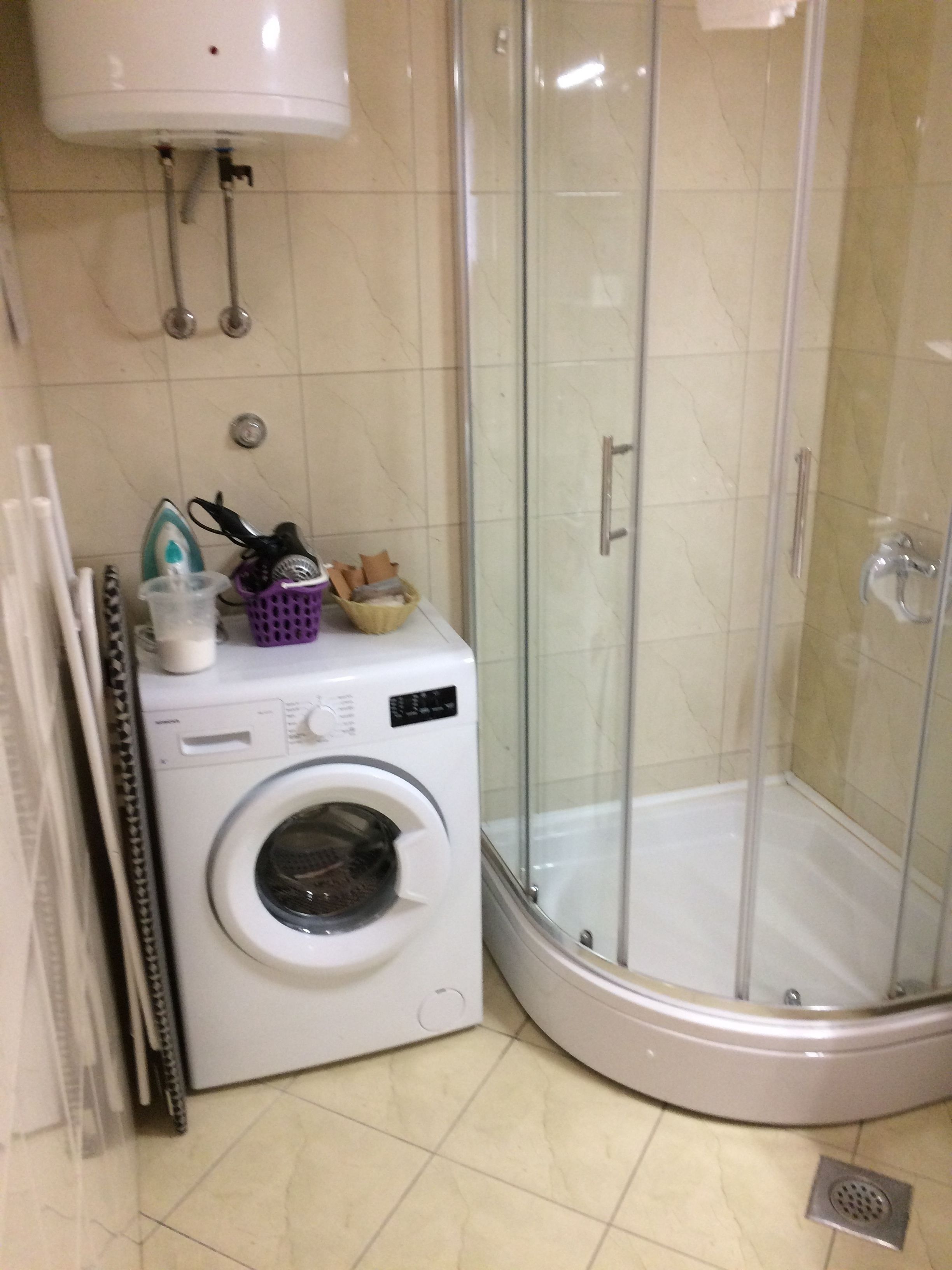 Ein Badezimmer im Eckbereich mit Waschmaschine, Duschkabine aus Glas und Fliesenboden.