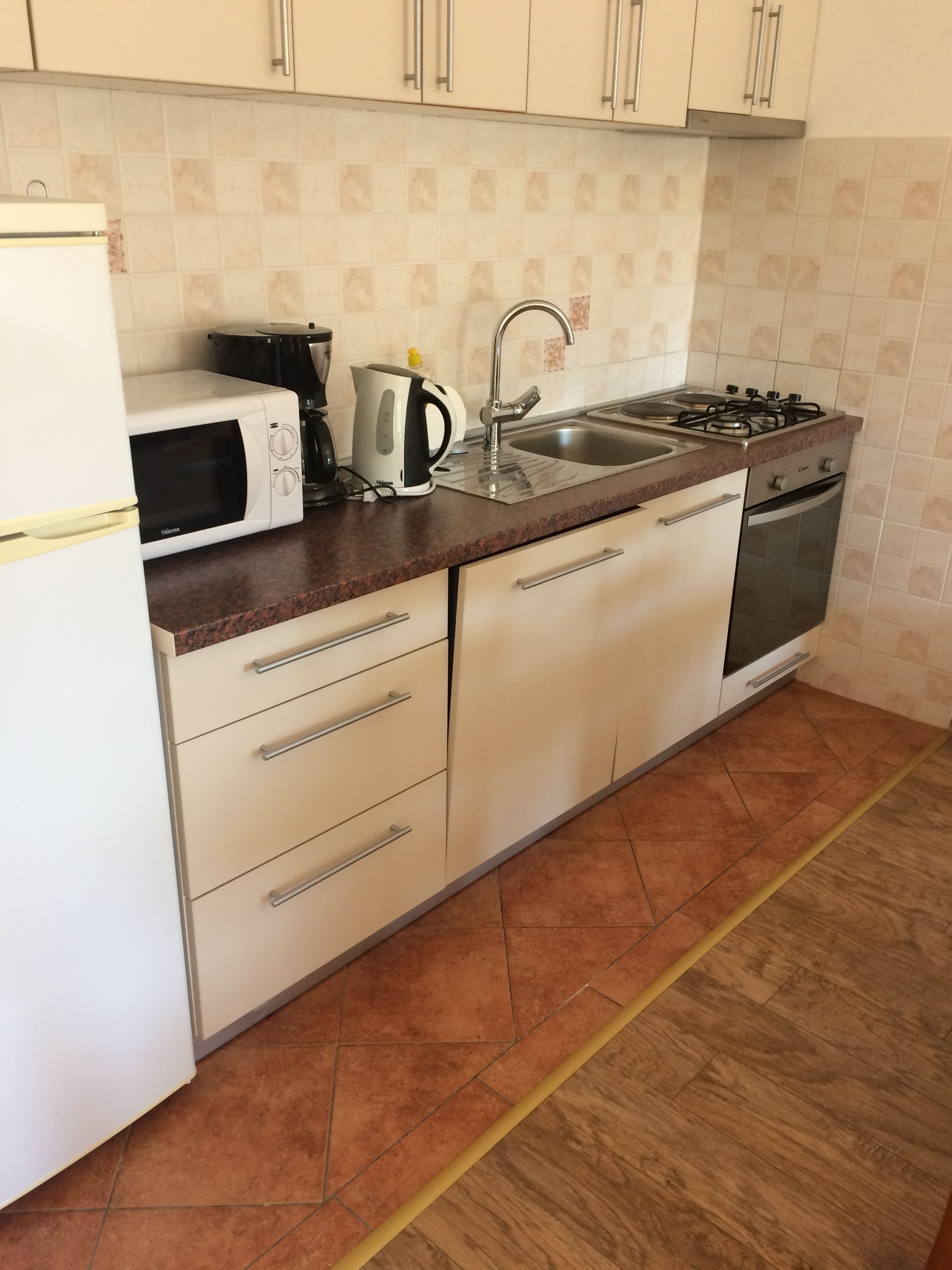 A kitchen with a microwave, kettle, sink, stove, and oven.
