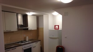 A compact kitchen with white cabinets, a gas stove, an oven, and a refrigerator. - Apartmani KLIM (Dubrovnik)
