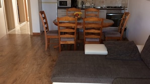 A living room with a sofa, wooden chairs, a dining table with a fruit bowl, and a kitchen area with cabinets and appliances. - Apartmani KLIM (Dubrovnik)