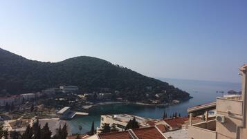 A coastal town with terracotta-roofed buildings, a marina, and a hilly backdrop.