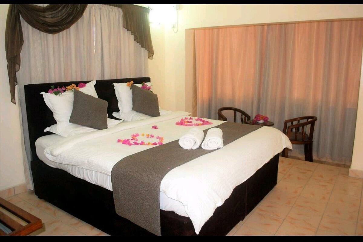 A neatly made bed with white linens, a dark headboard, and decorative pillows. There are two chairs and a small table in the room.