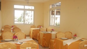 A dining area with tables set for four, each with a white tablecloth and orange chair covers. - Regency Inn (Mombasa)