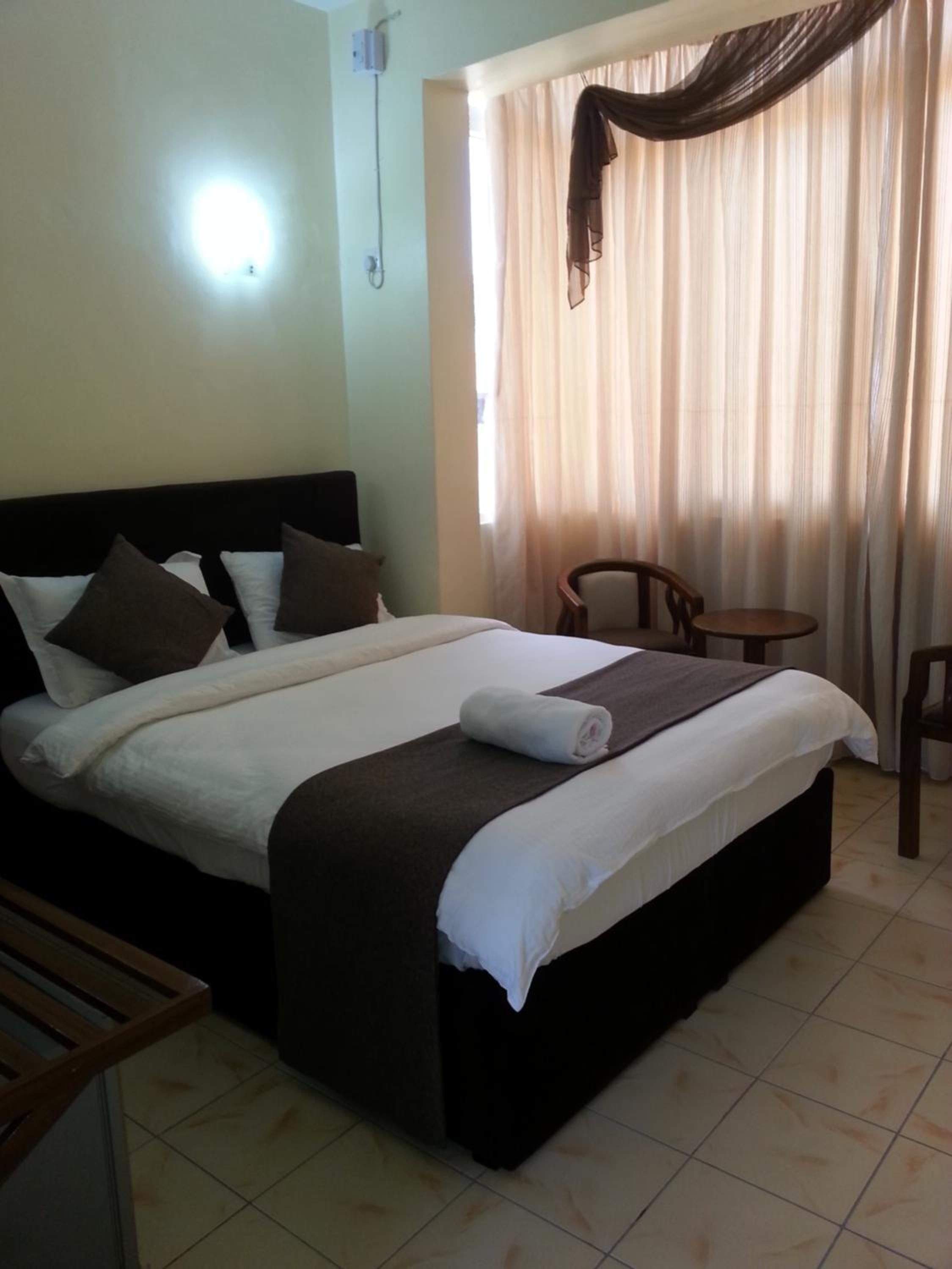 Una habitación de hotel con una cama, una mesita de noche, una silla y una ventana con cortinas.