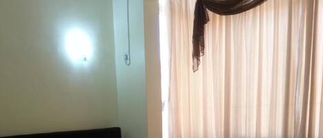 Una habitación de hotel con una cama, una mesita de noche, una silla y una ventana con cortinas.