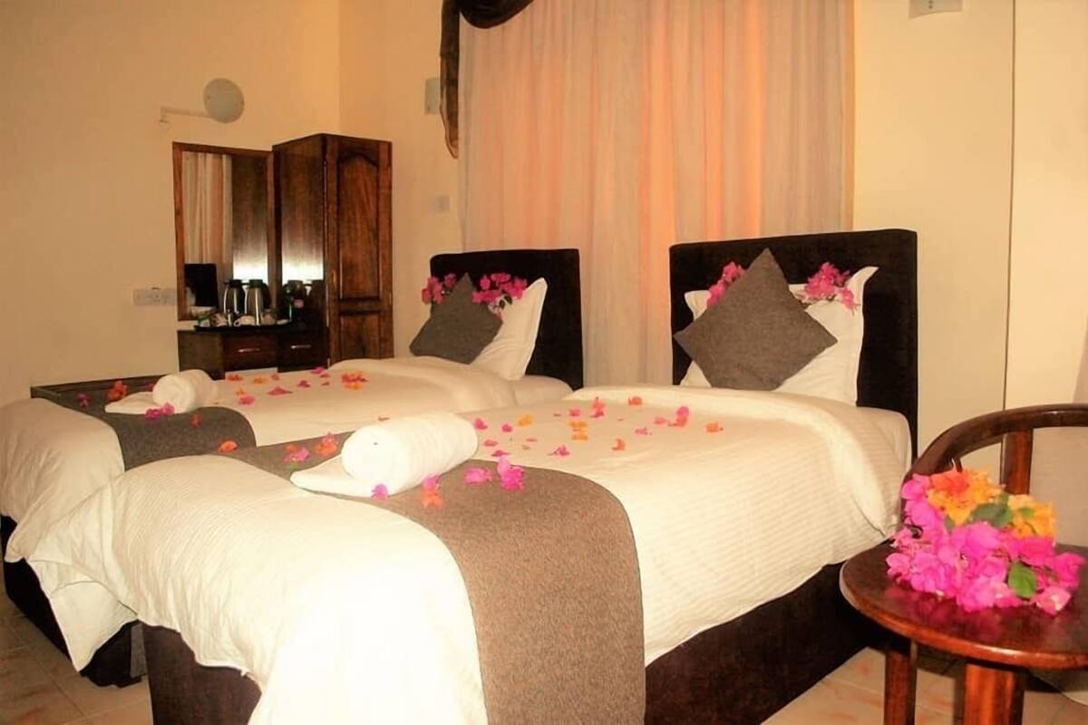 A hotel room with two beds, a mirror, a small table with flowers, and a curtain.