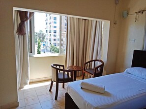 Een hotelkamer met een bed, een tafeltje, twee stoelen, een raam met gordijnen en uitzicht op gebouwen.