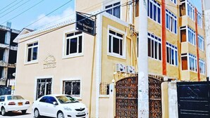 A multi-story building with a beige facade, a gated entrance, and a sign for 'The Regency Inn' with a contact number. - Regency Inn (Mombasa)
