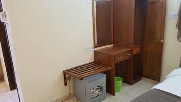 A small room with a wooden desk, a mirror, and a small trash bin.