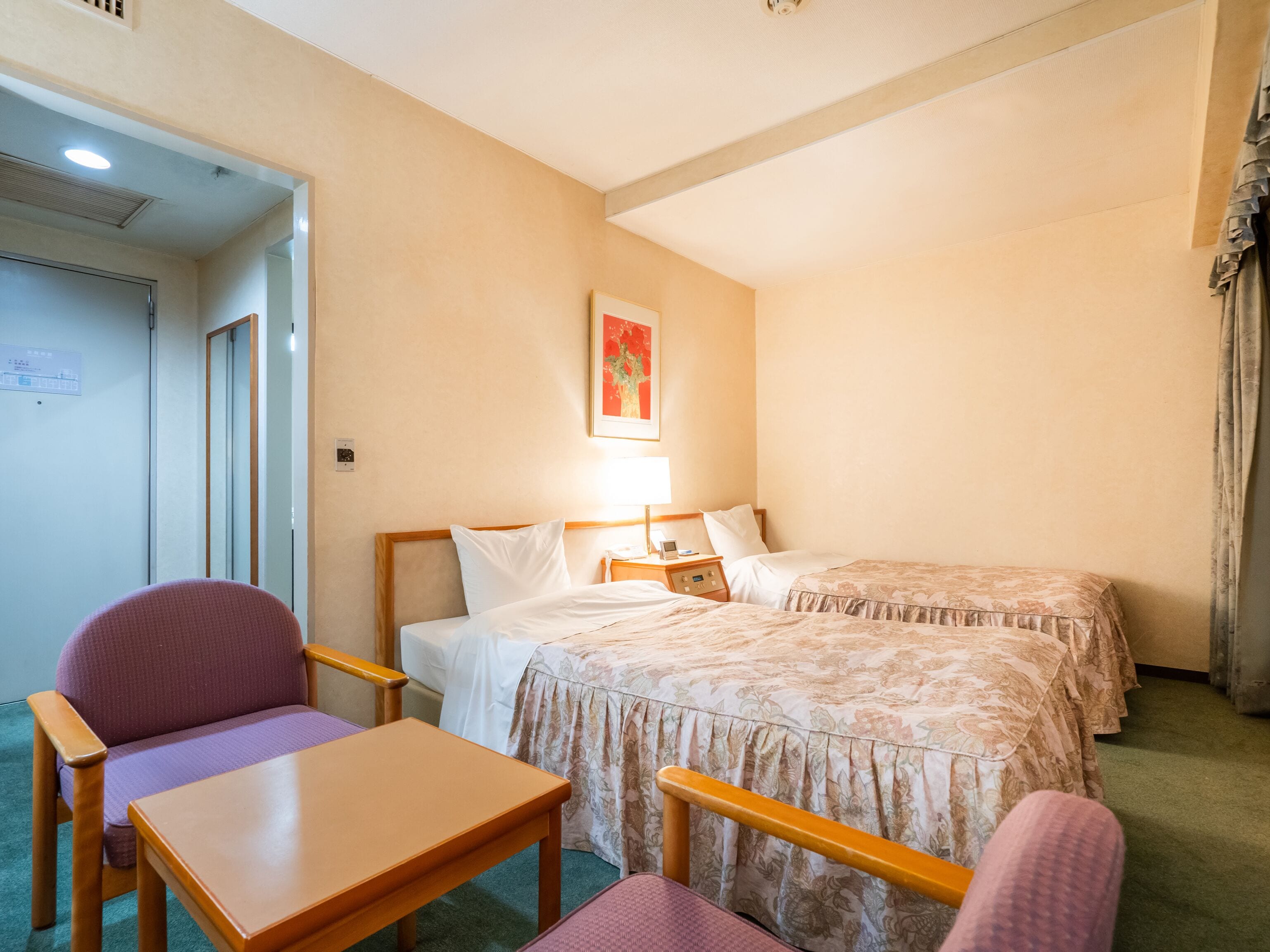 Een hotelkamer met twee bedden, een bureau, een stoel en een nachtkastje met lamp.