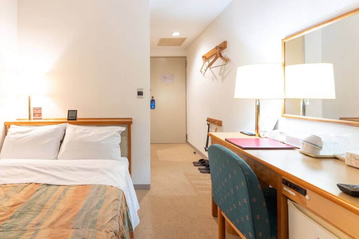 A hotel room with a bed, desk, chair, and a mirror.