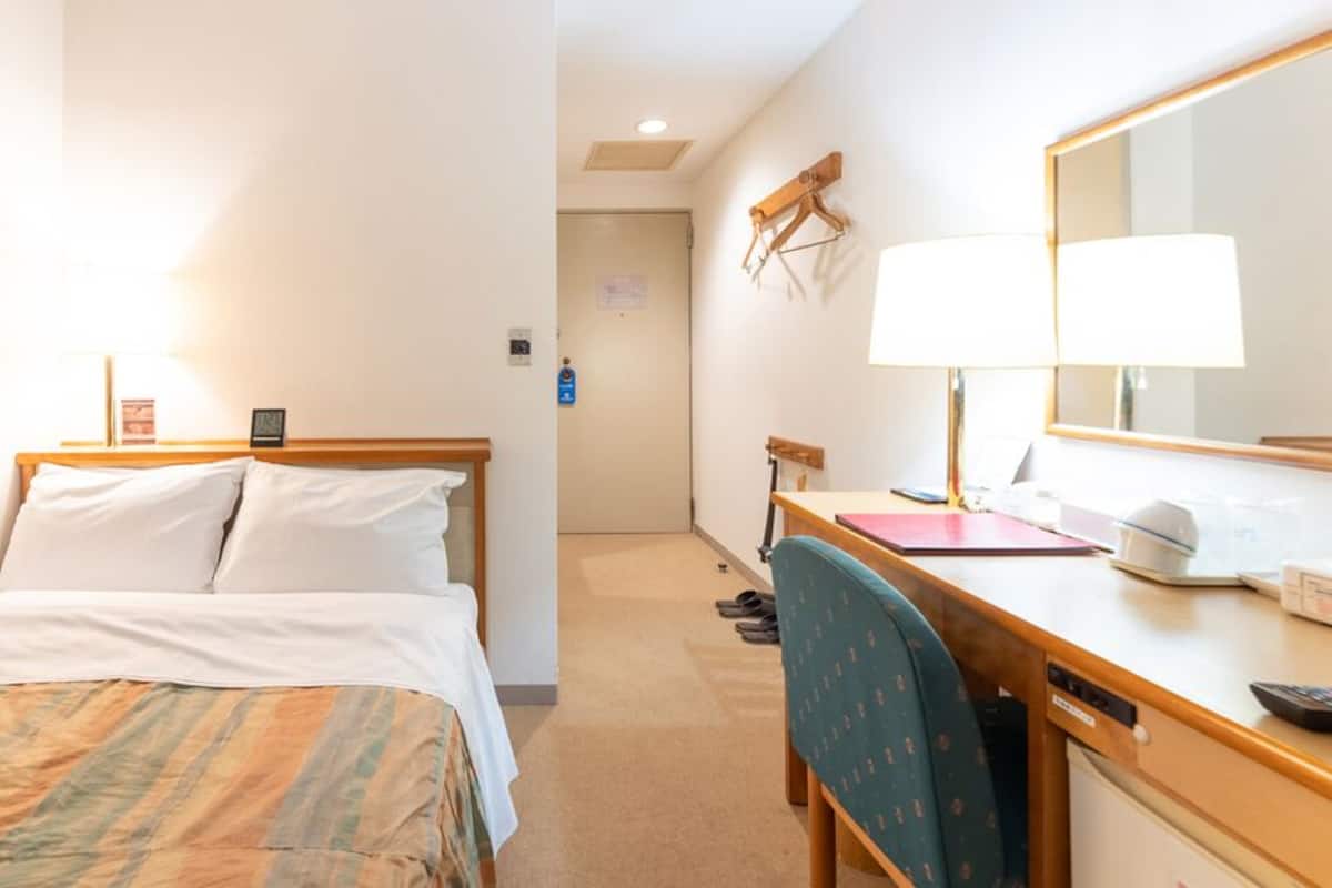 A hotel room with a bed, desk, chair, and a mirror.