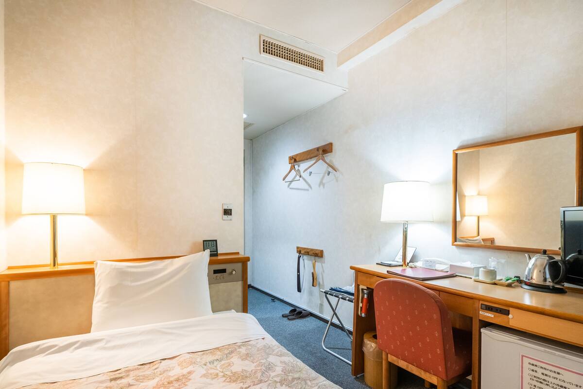 A hotel room with a bed, desk, chair, and a small kitchenette.