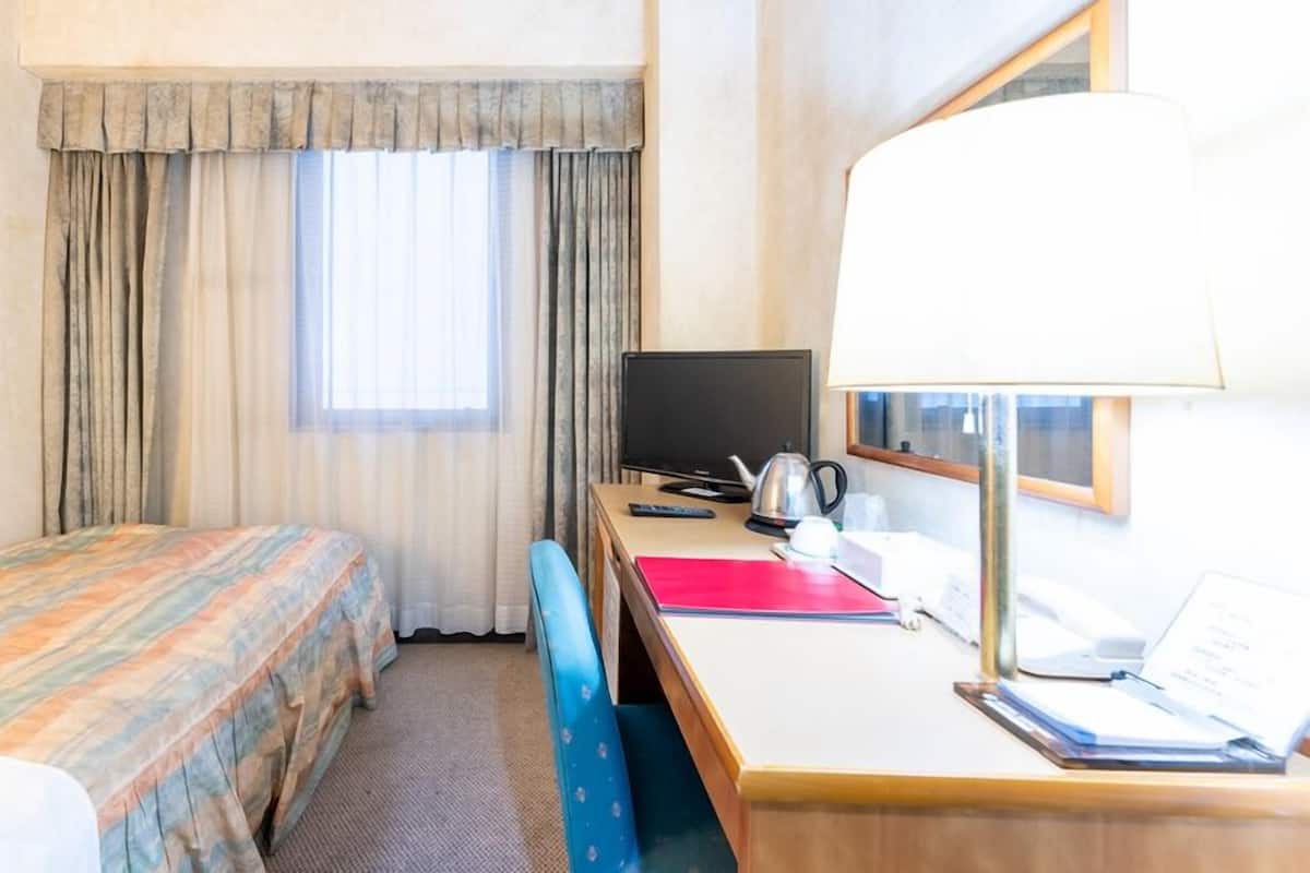 A hotel room with a bed, a desk with a computer, a lamp, and a window with curtains.