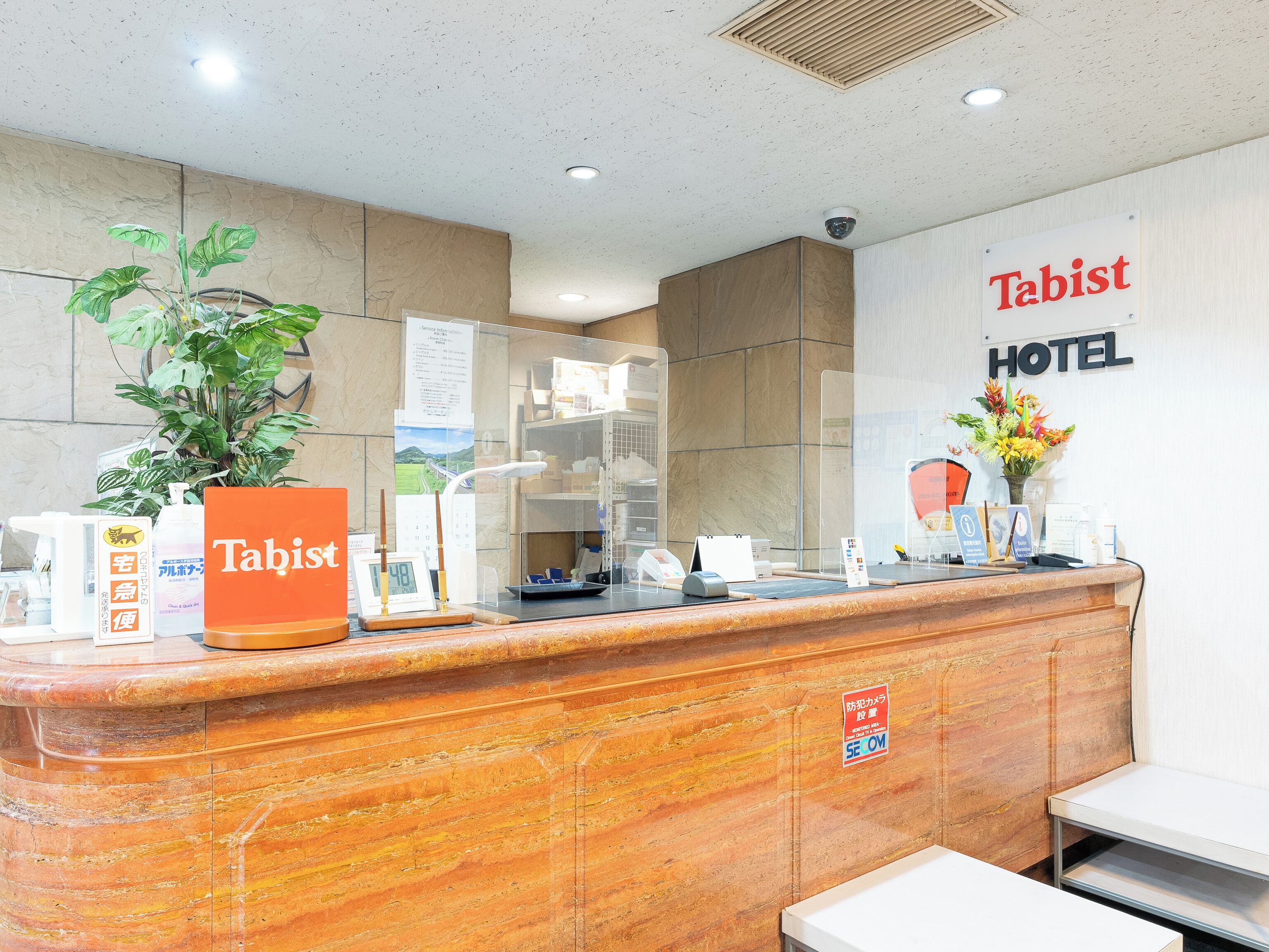 A hotel reception desk with a 'Tabist' sign, a plant, and a digital clock.