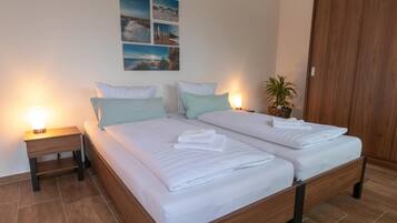 A double bed with white linens, two bedside tables with lamps, a wooden wardrobe, and a wall with four framed pictures.
