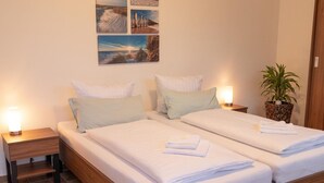Una cama doble con ropa de cama y almohadas blancas, dos mesitas de noche con lámparas, y una pared con tres cuadros enmarcados.