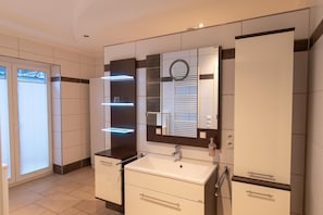 A modern bathroom with a large mirror, white cabinets, and a vanity with a sink. - Motel Am Bürgerpark (Werlte)