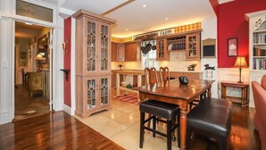A spacious kitchen with wooden cabinets, a dining table, and a red accent wall. - Meritage House - Excellent Location, King St. NOTL (Niagara-on-the-Lake)