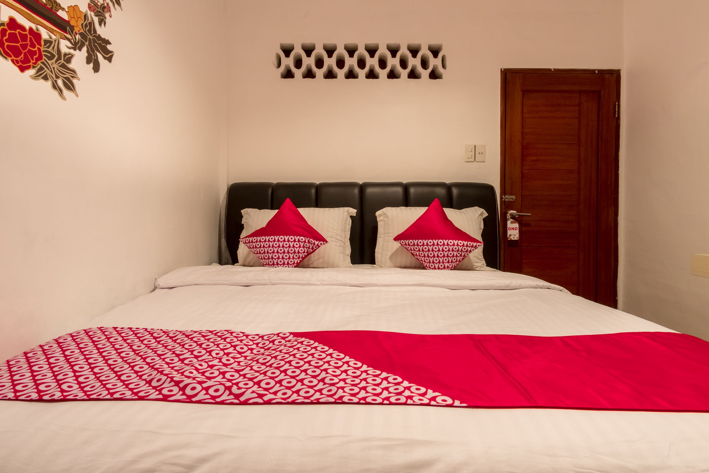 A neatly made bed with a red and white patterned bedspread, two red pillows, and a black headboard.