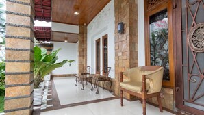 A well-lit indoor area with a stone pillar, a wooden chair, a small table, and a decorative door. - OYO 619 Naufal Guest House Syariah (Medan)
