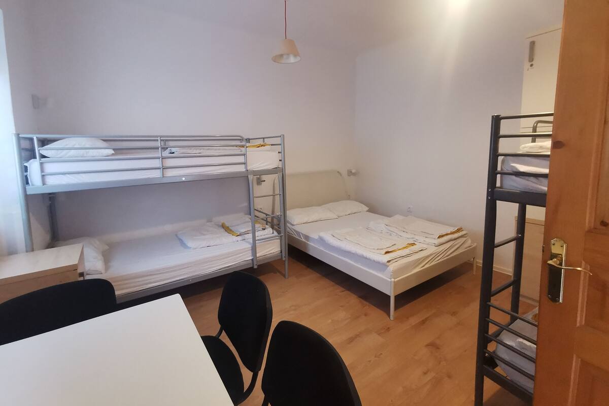 A dormitory room with bunk beds, a table, chairs, and a door.