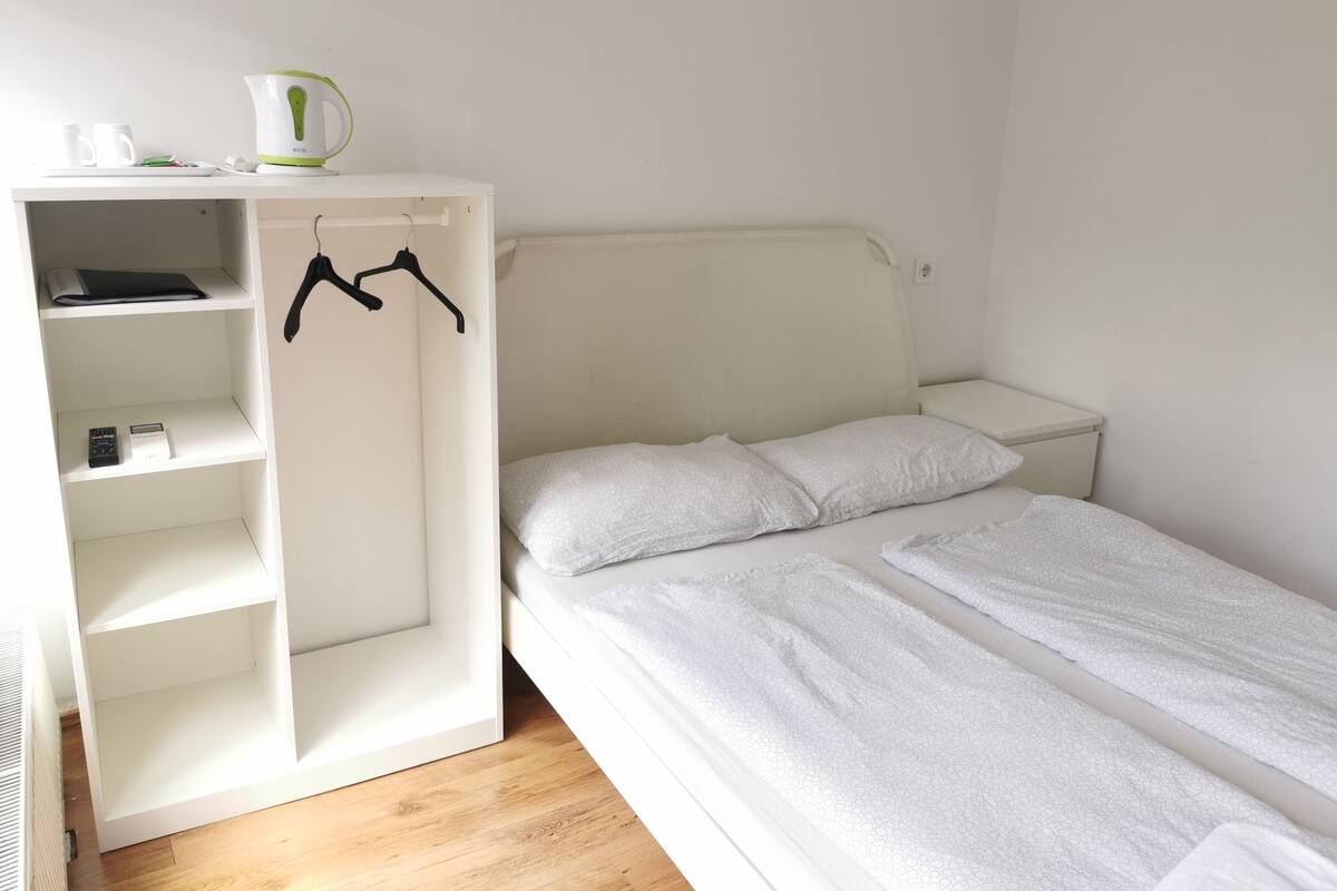 A bedroom with a bed, a white wardrobe, and a nightstand.