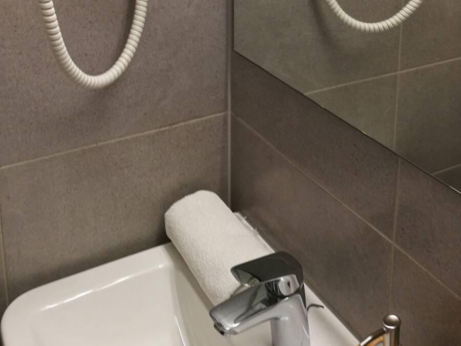 A bathroom with two hair dryers mounted on the wall, a sink with a faucet, and a towel dispenser.